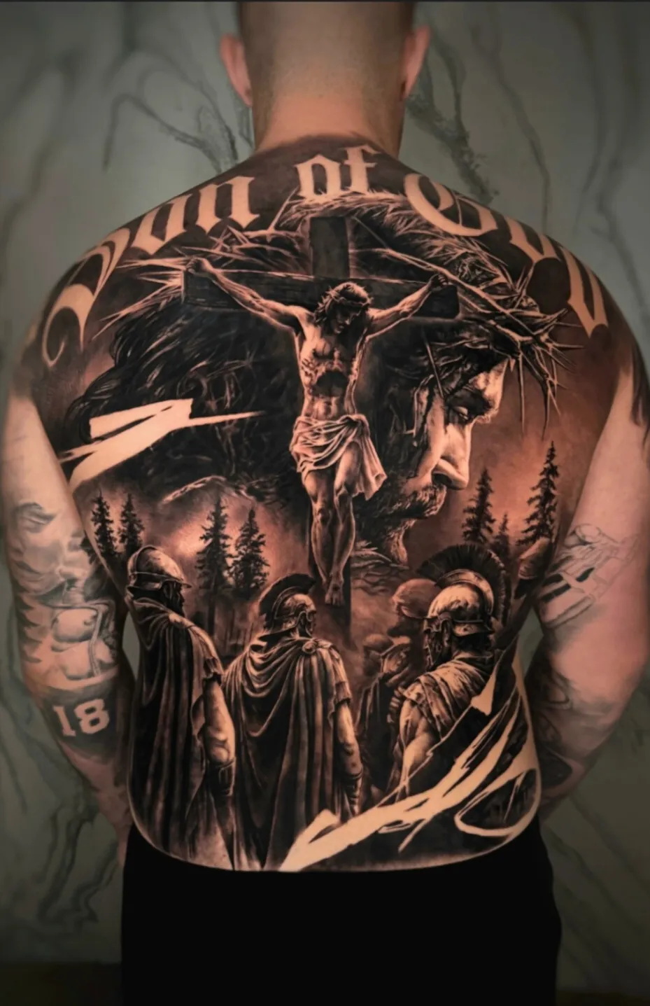 Espalda completa tatuada con escena de la crucifixión y soldados romanos, realismo en negro y gris
